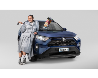 A person leaning against a blue Toyota car with a cracked windshield