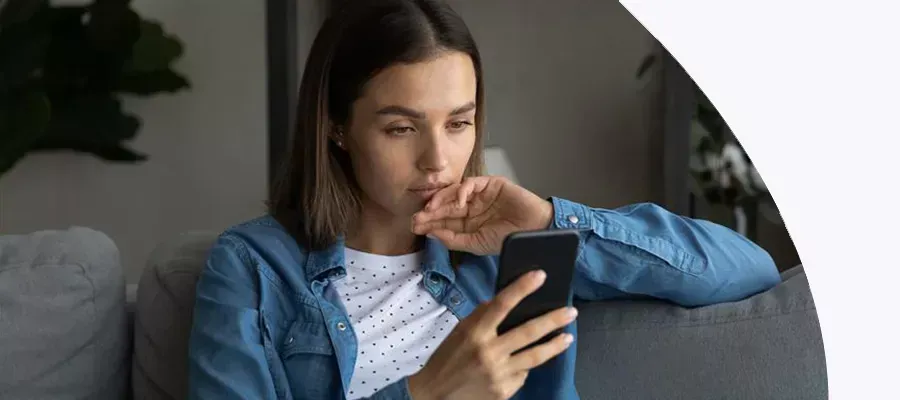 Serious woman sitting on sofa looking at smartphone and is upset